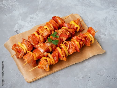 Uncooked marinated and rubbed chiken or turkey shish kebabs on skewers with onion, pepper and tomato ready for grilling or BBQ. Raw meat in a marinade with spices on cutting board. Soft focus