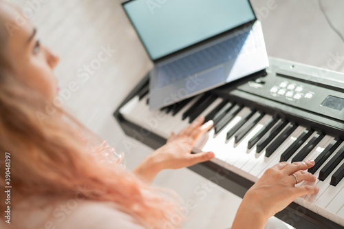 A woman watches video lessons on a digital tablet and plays on an electro synthesizer. The girl learns to play the piano remotely. © Михаил Решетников