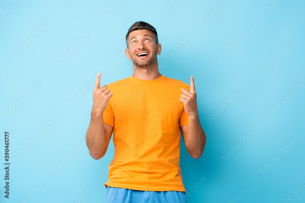 happy man in yellow t-shirt pointing with fingers and looking up on blue happy man in yellow t-shirt pointing with fingers and looking up on blue