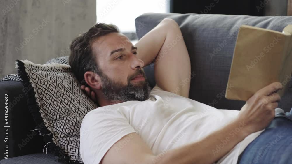 A relaxed man reading a book on the sofa at home A relaxed man reading a book on the sofa at home