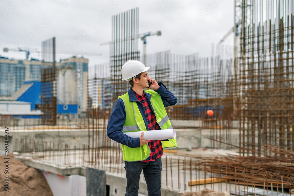 Builder in a white helmet with a drawing in his hands on the background of the construction site Builder in a white helmet with a drawing in his hands on the background of the construction site