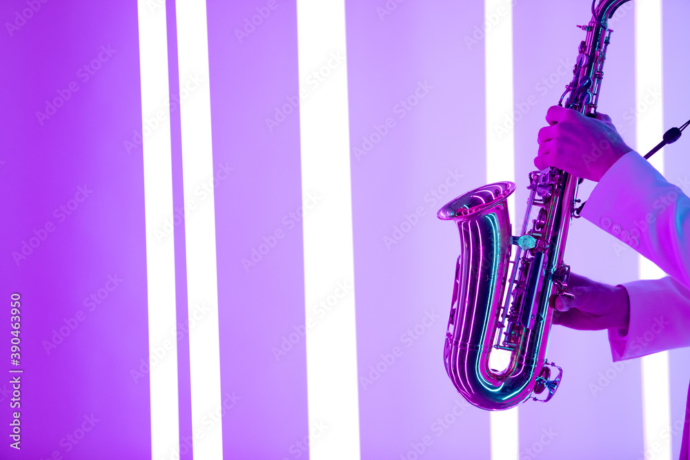 Fototapeta premium Male hands are holding a shiny saxophone against the background of neon lamps.