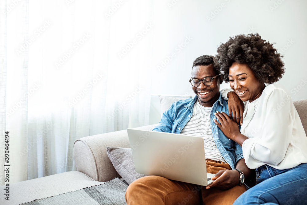 Attractive couple using laptop together on sofa to shop online at home in the living room. Attractive couple using laptop together on sofa at home in the living room Attractive couple using laptop together on sofa to shop online at home in the living room. Attractive couple using laptop together on sofa at home in the living room