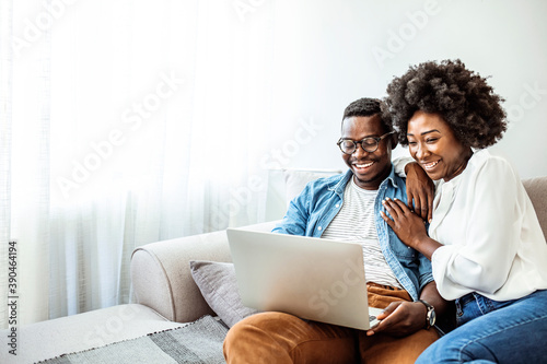 Attractive couple using laptop together on sofa to shop online at home in the living room. Attractive couple using laptop together on sofa at home in the living room