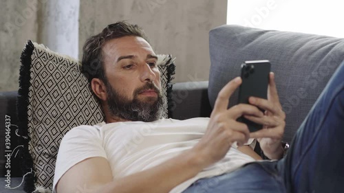 A relaxed man using mobile phone on the sofa at home 