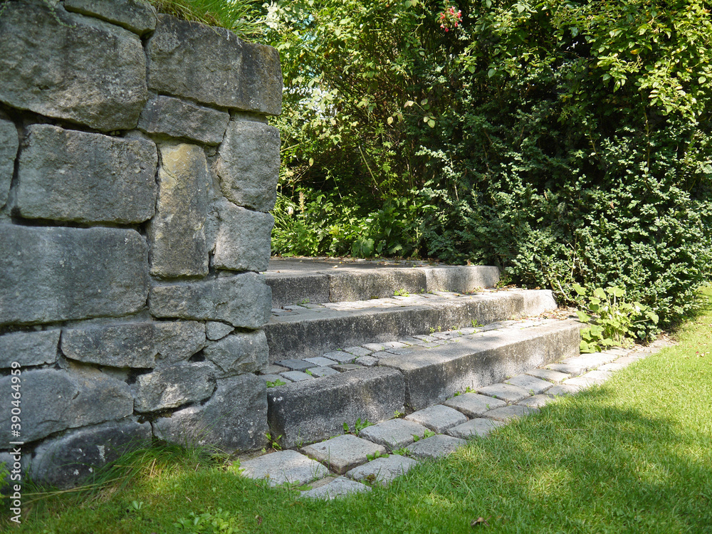 Old stone steps in the park. Lawn and trees. Landscaping. Support wall.
