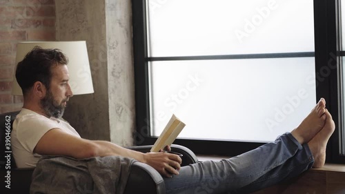 A relaxed man reading a book on the sofa at home 