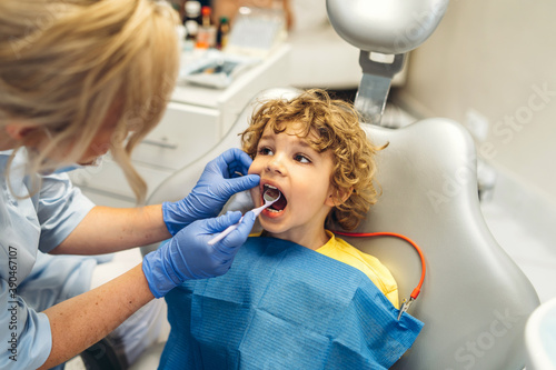 Cute young boy visiting dentist, having his teeth checked by female dentist in dental office.