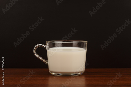 Glass cup of milk on dark wooden table with black background