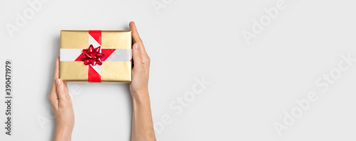 New Year and Christmas 2021 banned. Golden gift with prohibiting red and white tape in female hands on gray background flat lay top view. Holidays in quarantine. Coronavirus 2019-nCoV. Stay at home