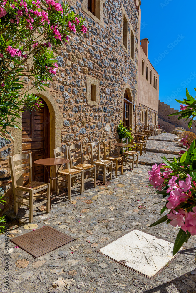 Traditional cafe exterior in the fortified medieval  castle of Monemvasia. Iron tables and wooden chairs with the view of the  aegean sea in the background.