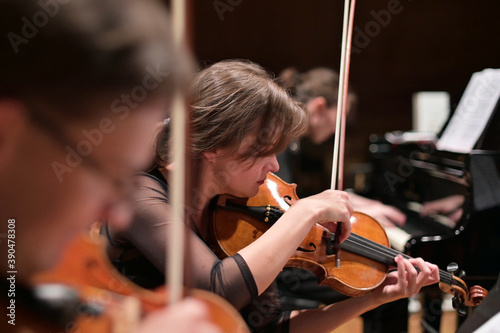 Focus on a young woman playing the violin with a string quartet and grand piano