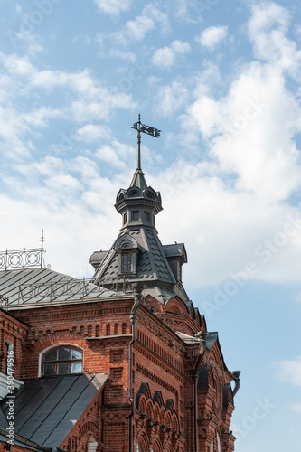 fragment of the upper part of the historical building with a tower shows the beauty of brick sacred architecture. Metal weather vane on the roof of the tower
