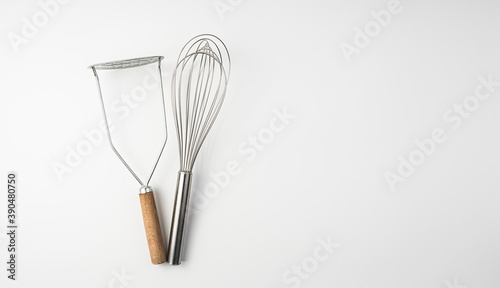 The whisk and the potato masher on white background.Culinary background, top view.