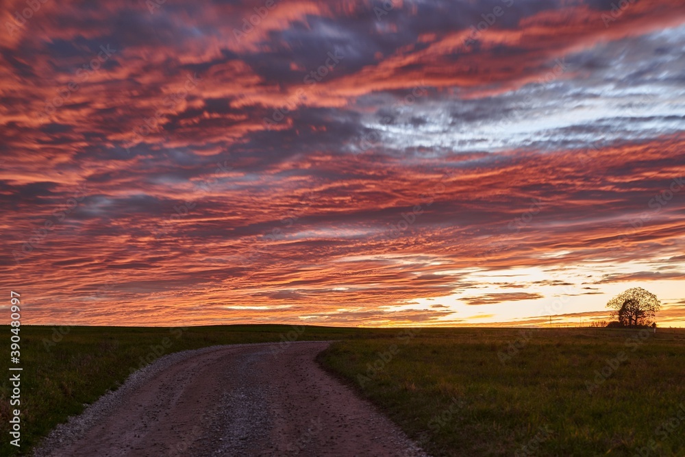 Long exposure of a dramatic sunset on a lonely field. Sunset with red clouds on a green meadow.