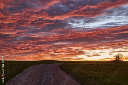 Long exposure of a dramatic sunset on a lonely field. Sunset with red clouds on a green meadow.