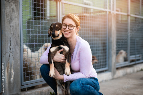 Young adult woman holding adorable dog in animal shelter. photo