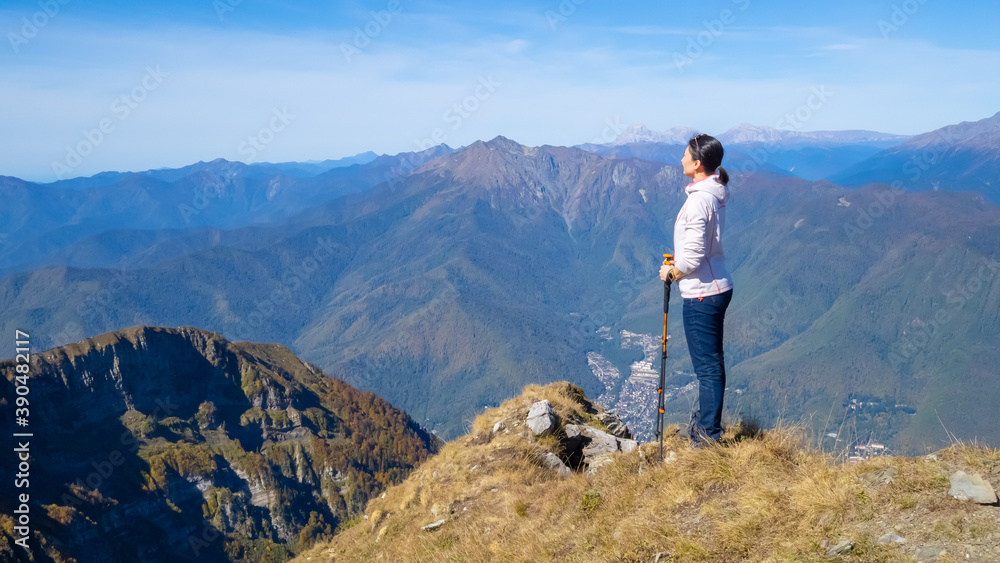Woman hiker goes hiking, stands on top of mountain and looks at autumn nature mountains landscape in sunny weather. Outdoor activities. Copy space, back view