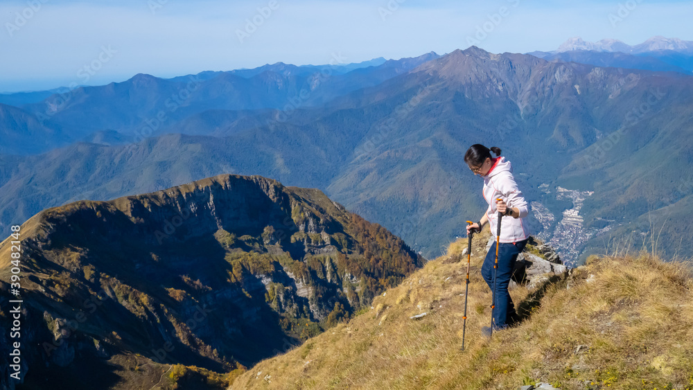 Woman hiker goes hiking, stands on top of mountain and looks at autumn nature mountains landscape in sunny weather. Outdoor activities. Copy space, back view