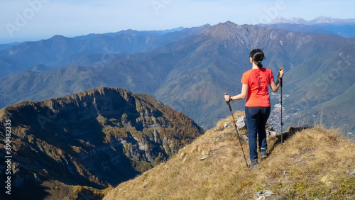 Woman hiker goes hiking, stands on top of mountain and looks at autumn nature mountains landscape in sunny weather. Outdoor activities. Copy space, back view