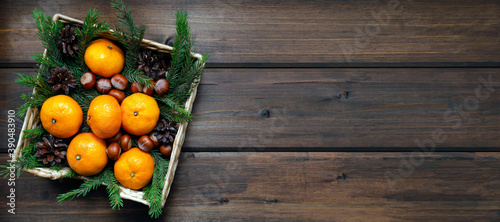 banner new year concept. juicy tangerines fir branches, cones, nuts in a wicker basket on a tein wooden aged background with plenty of space for text