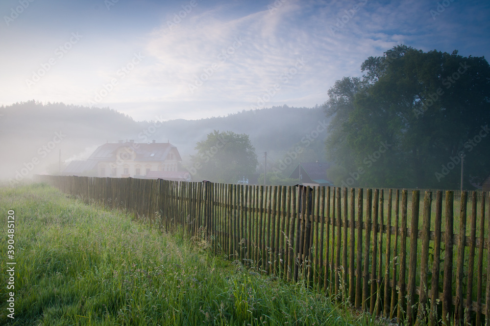 village in foggy morning, fence and trees covered by autumn weather