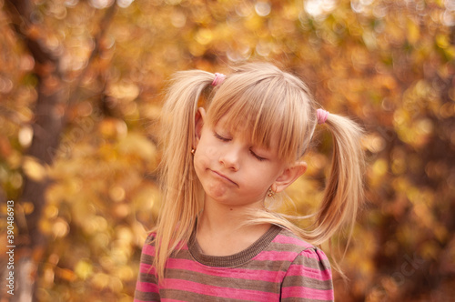 Portrait of a blonde girl with closed eyes in an autumn park. Tired child.