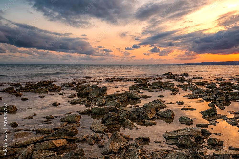 Stone beach at sunset. Twilight sea and sky. Dramatic sky and clouds. Nature landscape.