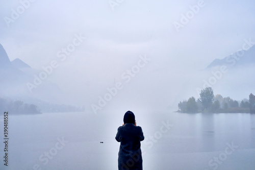 A person staring at a cloudy lake during a cold autumn day