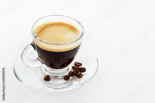 Transparent cup of espresso on a white background. There are coffee beans on the saucer. Space for text.