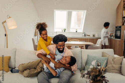 Afro father and his children bonding at home. They are laughing and tickling together