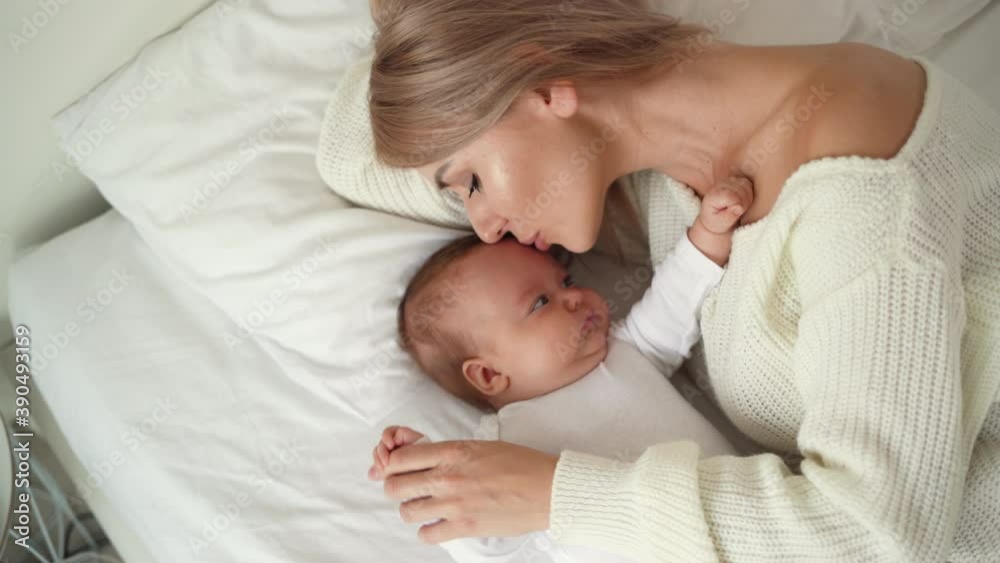 An overhead view of a mother and her newborn baby boy kissing and hugging while relaxing in bed after breastfeeding. Happy motherhood and fatherhood concept. An overhead view of a mother and her newborn baby boy kissing and hugging while relaxing in bed after breastfeeding. Happy motherhood and fatherhood concept.