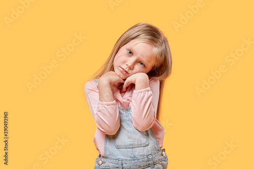 Portrait of a little sad blonde girl looking at the camera. Yellow isolated background.