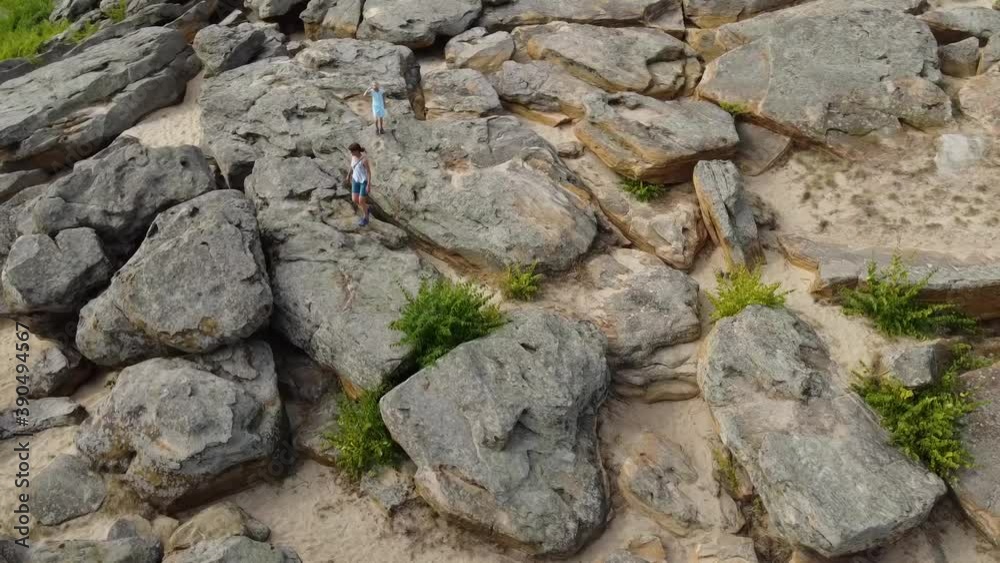 Aerial view. Mom and child walk and climb a cluster of large stones. Sand is visible between the stones. Sunny day. Aerial view. Mom and child walk and climb a cluster of large stones. Sand is visible between the stones. Sunny day.
