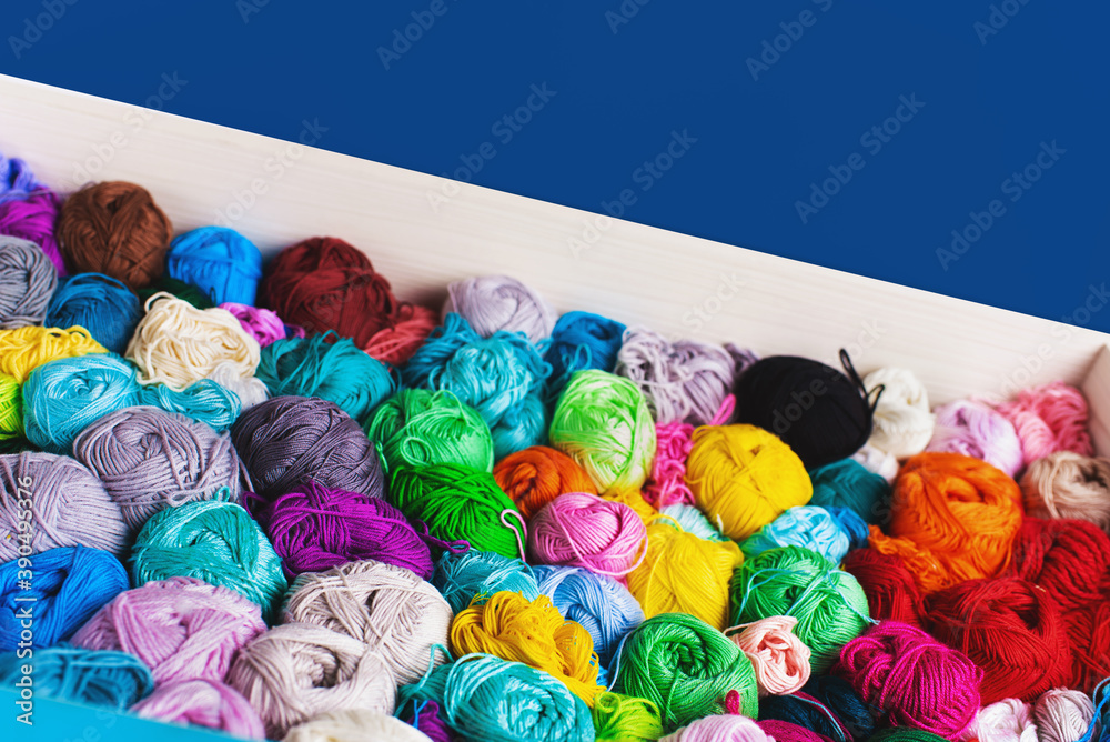 Сrocheting and knitting. Colorful multicolored skeins of yarn in the box on a blue background. Women's hobby.	