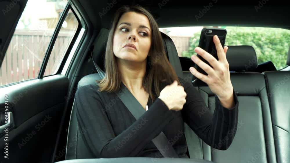 Beautiful woman sitting in car checking makeup and hair looking in cell phone Beautiful woman sitting in car checking makeup and hair looking in cell phone