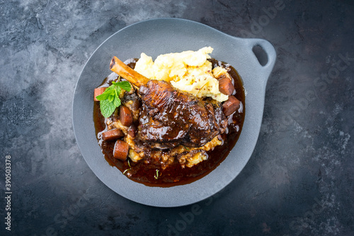 Modern style traditional braised slow cooked lamb shank in red wine sauce with shallots and mashed potatoes offered as top view in a design cast iron plate with copy space photo