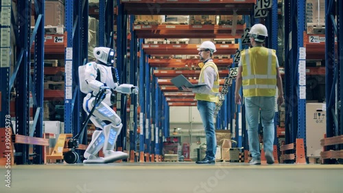 Storeman checking operation of robot pulling a cart