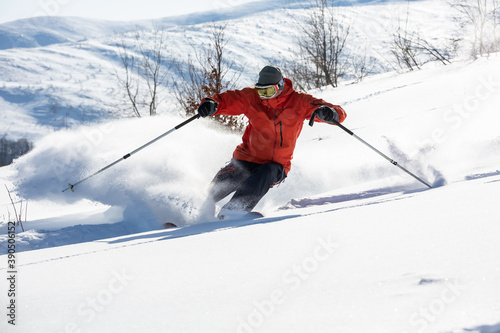A skier is in the deep snow. Sunny winter day. A skier is wearing red jacket. 
