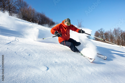 A skier is in the deep snow. Sunny winter day. A skier is wearing red jacket.	
