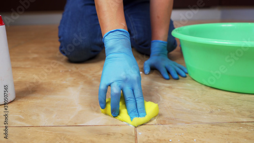 Blue-gloved hands scrub the marble floor using a sponge and detergent.