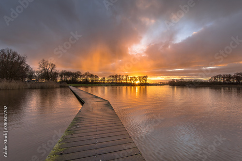 Wooden walkway in lake under orange sunset © creativenature.nl