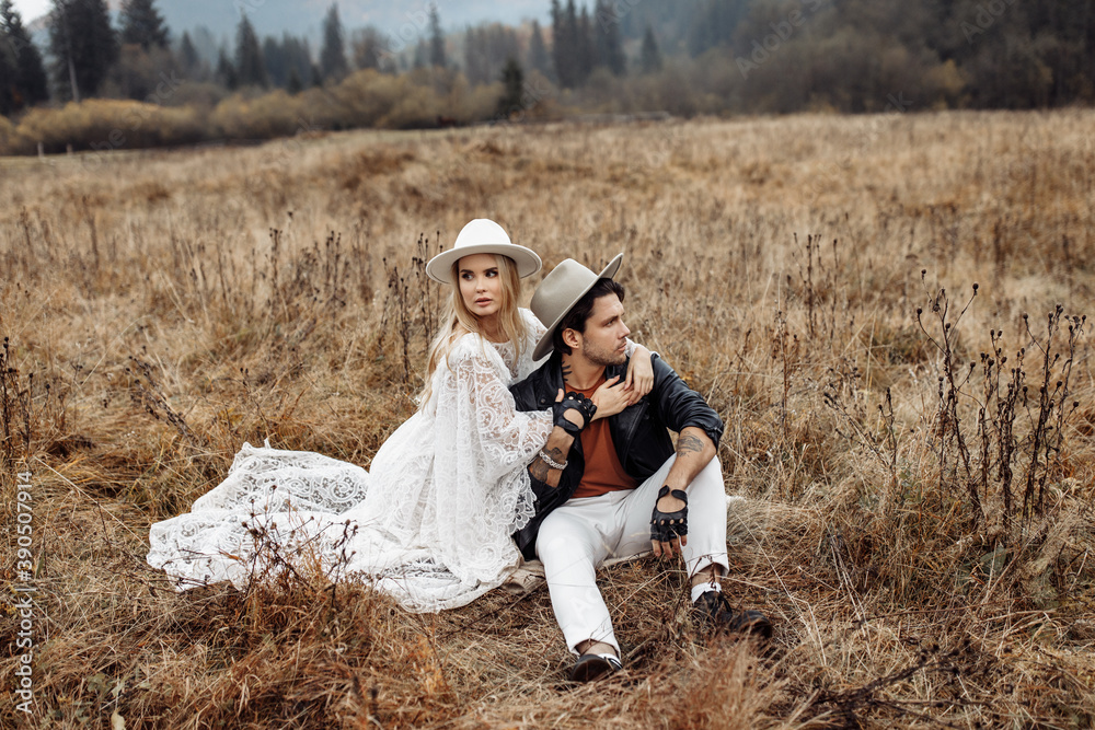 Stylish couple on a walk at the field, wearing a hats, handsome man and beautiful woman sit on the grass, loving husband spend time with adorable wife, togetherness concept Stylish couple on a walk at the field, wearing a hats, handsome man and beautiful woman sit on the grass, loving husband spend time with adorable wife, togetherness concept