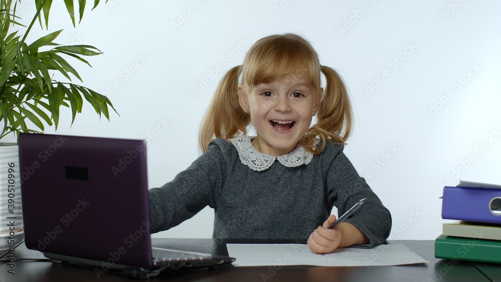 Child schoolgirl learns lessons at home sitting at table using digital laptop computer. Portrait of kid girl distance education. Studying during coronavirus quarantine. White background Child schoolgirl learns lessons at home sitting at table using digital laptop computer. Portrait of kid girl distance education. Studying during coronavirus quarantine. White background