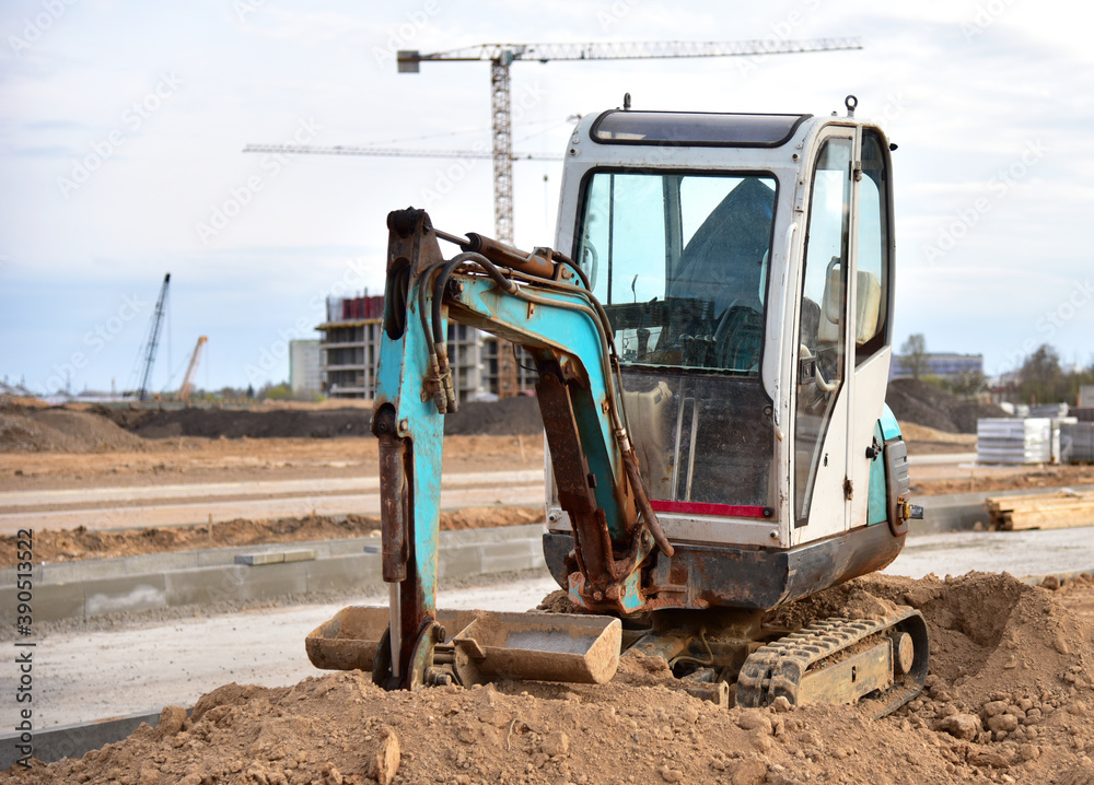 Mini excavator digg trench to lay cables concrete curbs and paving slabs at construction site. Backhoe on earthwork/roadworks Mini excavator digg trench to lay cables concrete curbs and paving slabs at construction site. Backhoe on earthwork/roadworks