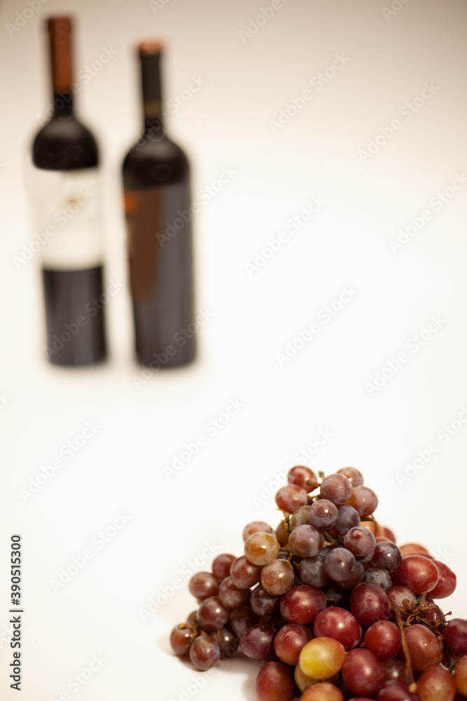 Obraz premium Champagne grape and Red Globe grape in front with 2 blurred wine bottles in the background on a white background.
