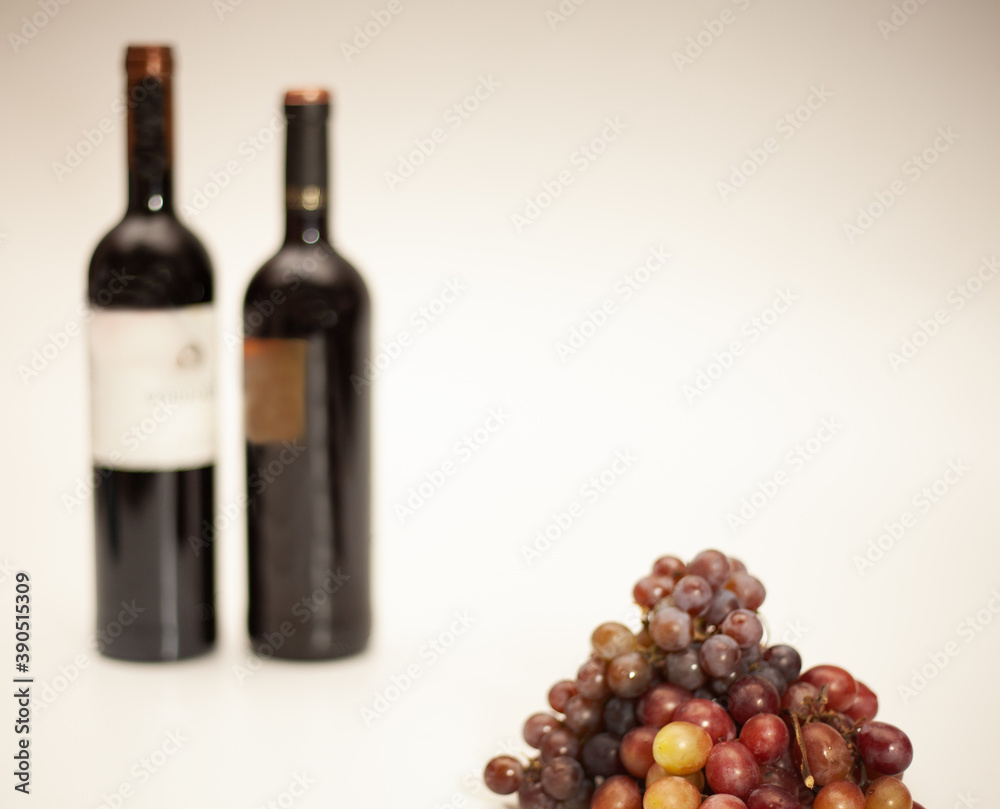 Obraz premium Champagne grape and Red Globe grape in front with 2 blurred wine bottles in the background on a white background.