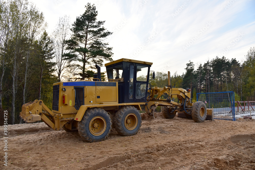 Motor Grader on road construction in forest area. Greyder leveling the sand, ground and gravel during road work. Heavy machinery and construction equipment for grading. Earthworks grader machine Motor Grader on road construction in forest area. Greyder leveling the sand, ground and gravel during road work. Heavy machinery and construction equipment for grading. Earthworks grader machine