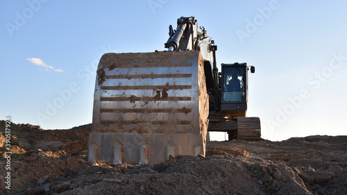Excavator working on earthmoving at open pit mining. Backhoe digs sand and gravel on blue sky background. Heavy construction equipment for quarrying. Excavation at construction site.
