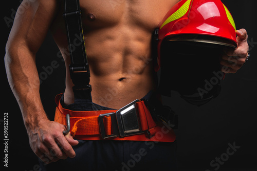 muscular, handsome young firefighter on dark background holding fire helmet, healthy lifestyle concept